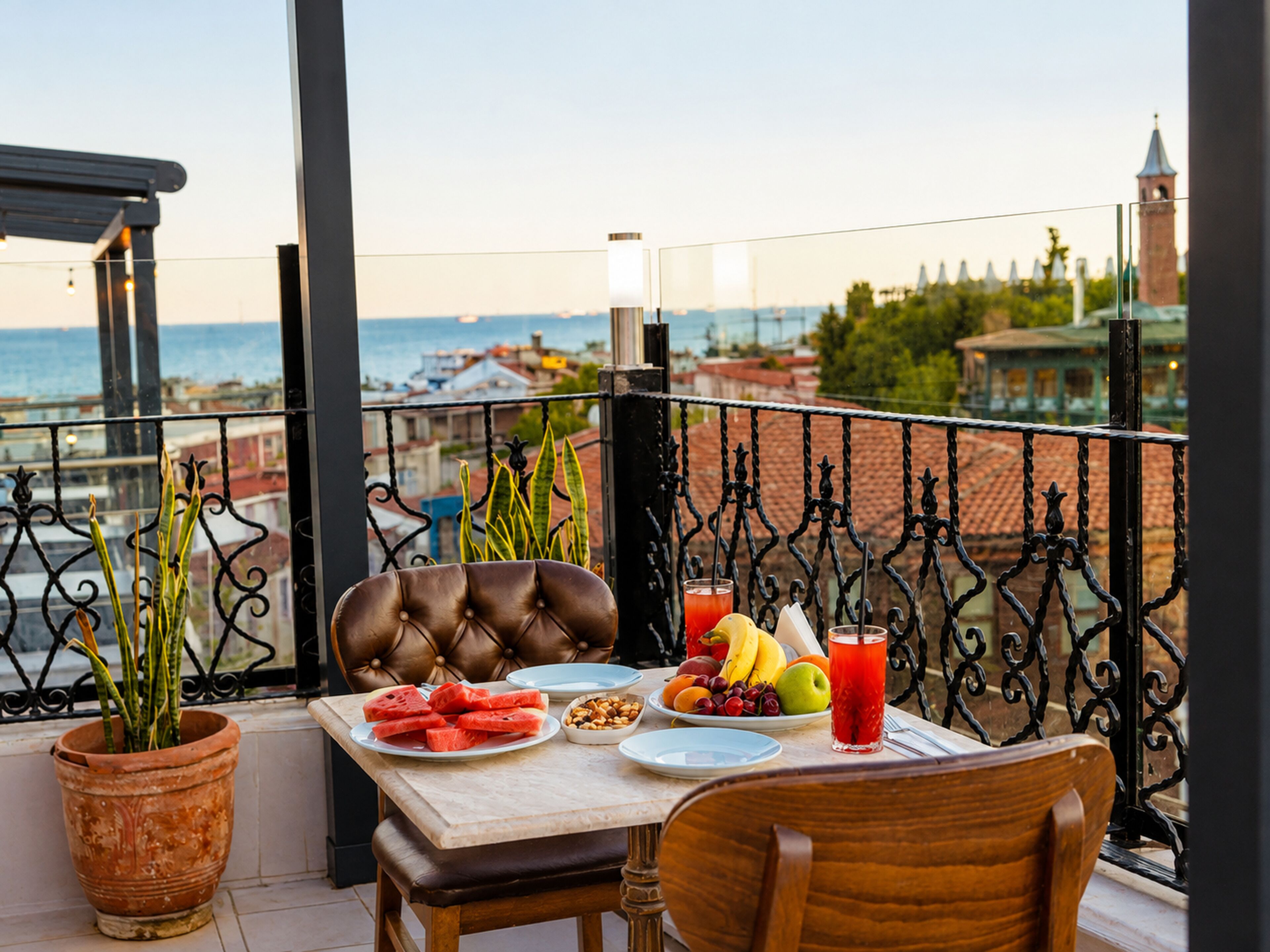 A balcony with a table set for two, featuring a variety of fruits and a glass of red beverage.