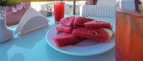 A table with a plate of watermelon slices, a glass of red beverage, and a vase with flowers.