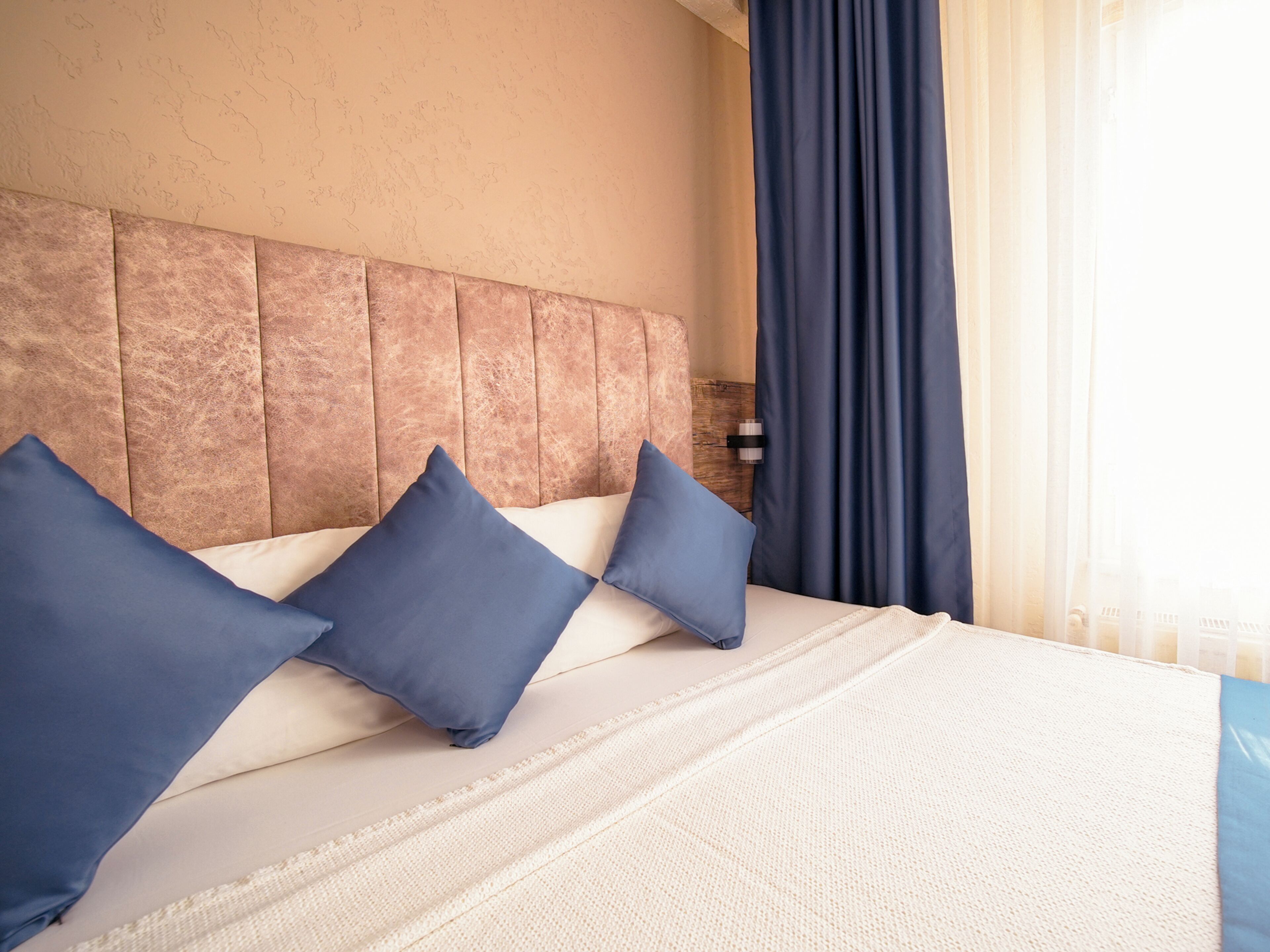 Una habitación de hotel con una cama grande, cabecera y ventana con cortinas.
