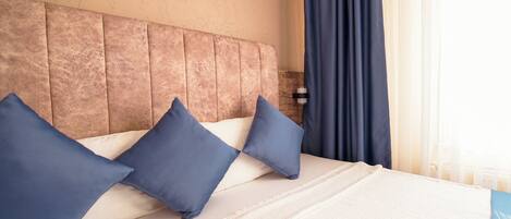 Una habitación de hotel con una cama grande, cabecera y ventana con cortinas.