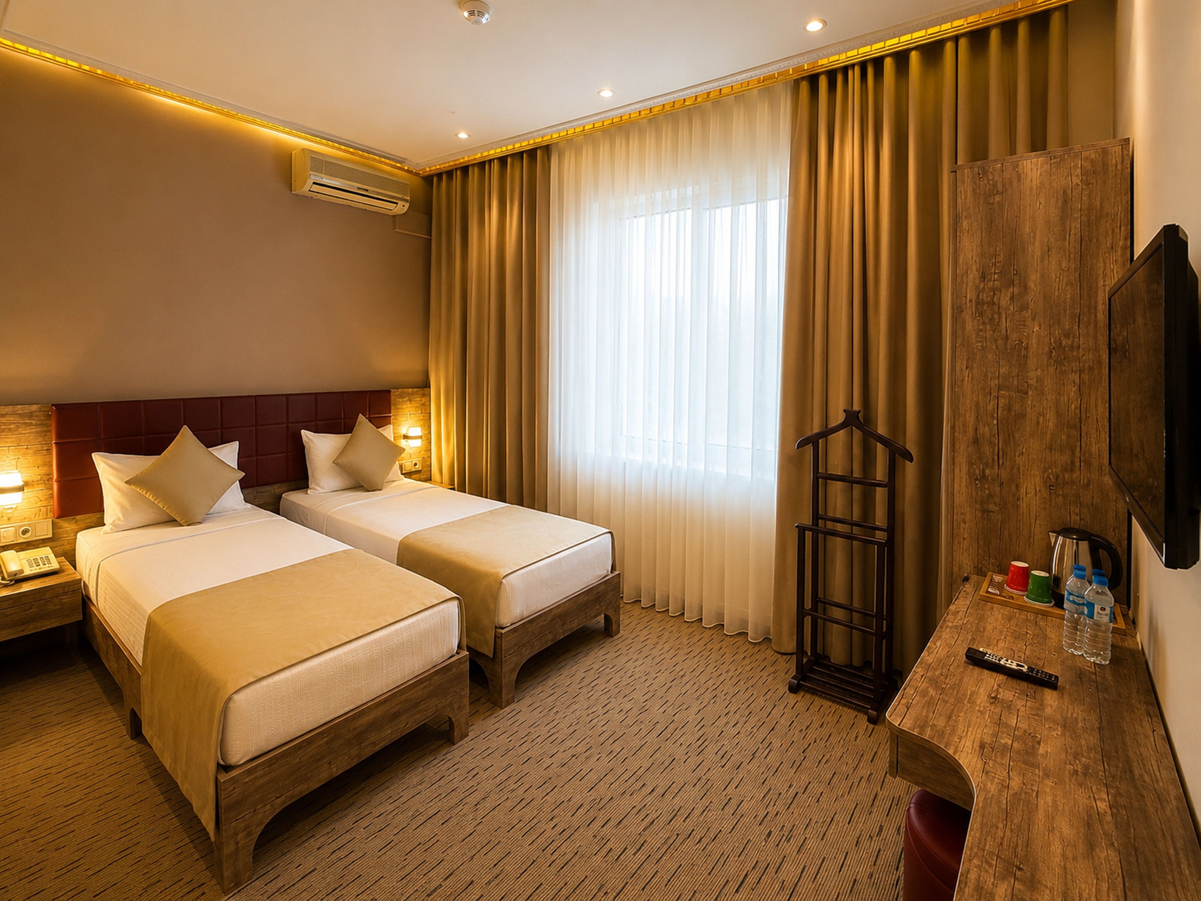 A hotel room with two beds, a wooden desk, a hanging coat rack, and a television.