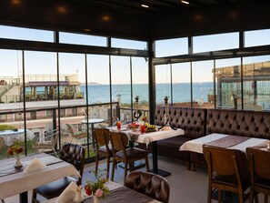 A restaurant with a view of the sea, featuring tables and chairs, a bar area, and a seating section with a high backrest. - Grand Ambiance Hotel (Istanbul)