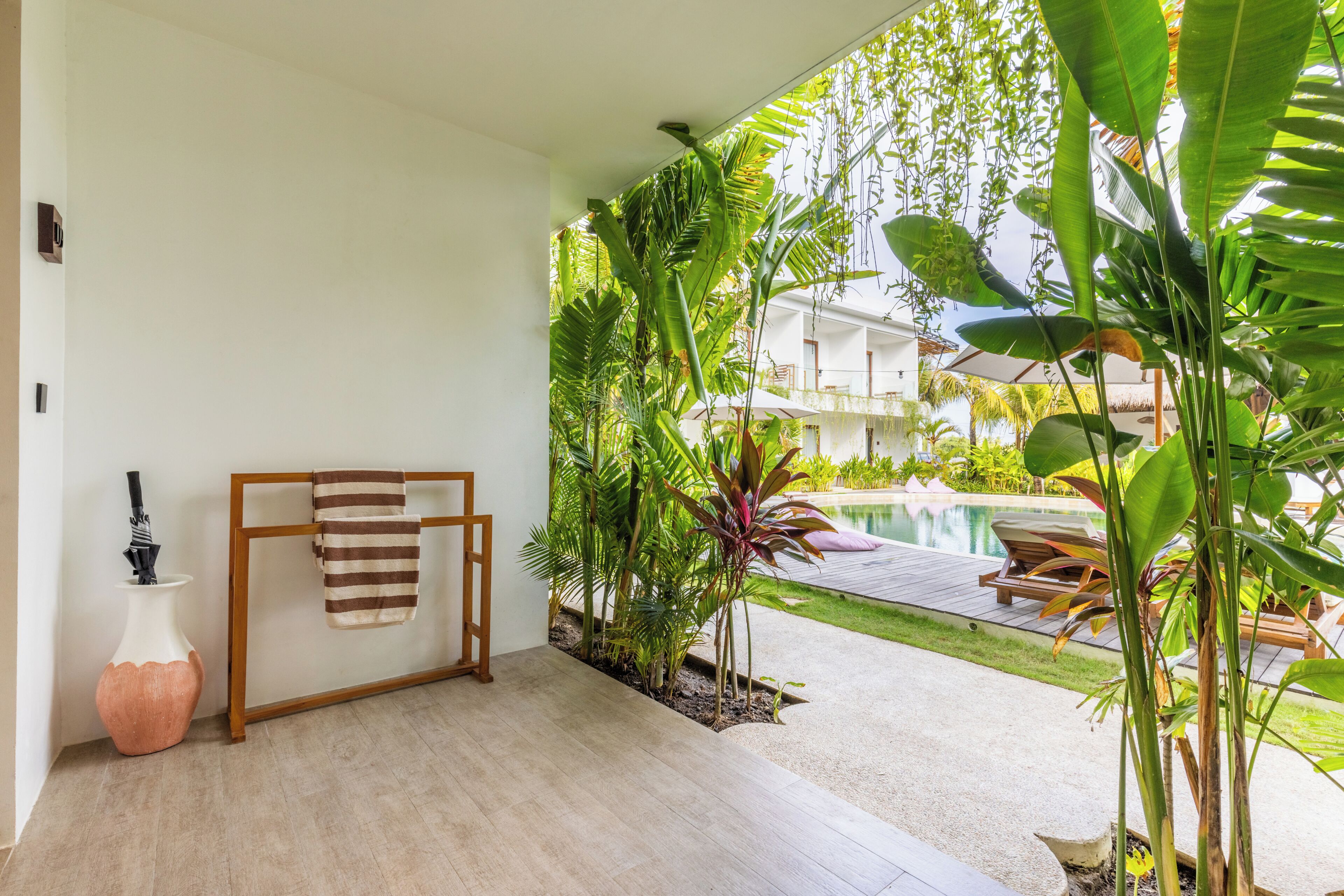 A room with a wooden floor, a towel rack, a vase, and a view of a pool and greenery.