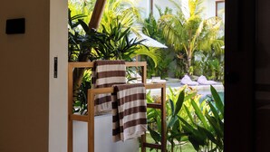 A room with a wooden bench, a thatched roof, and a view of a pool and palm trees. - Uryah Hotel Lombok (Selong Belanak)
