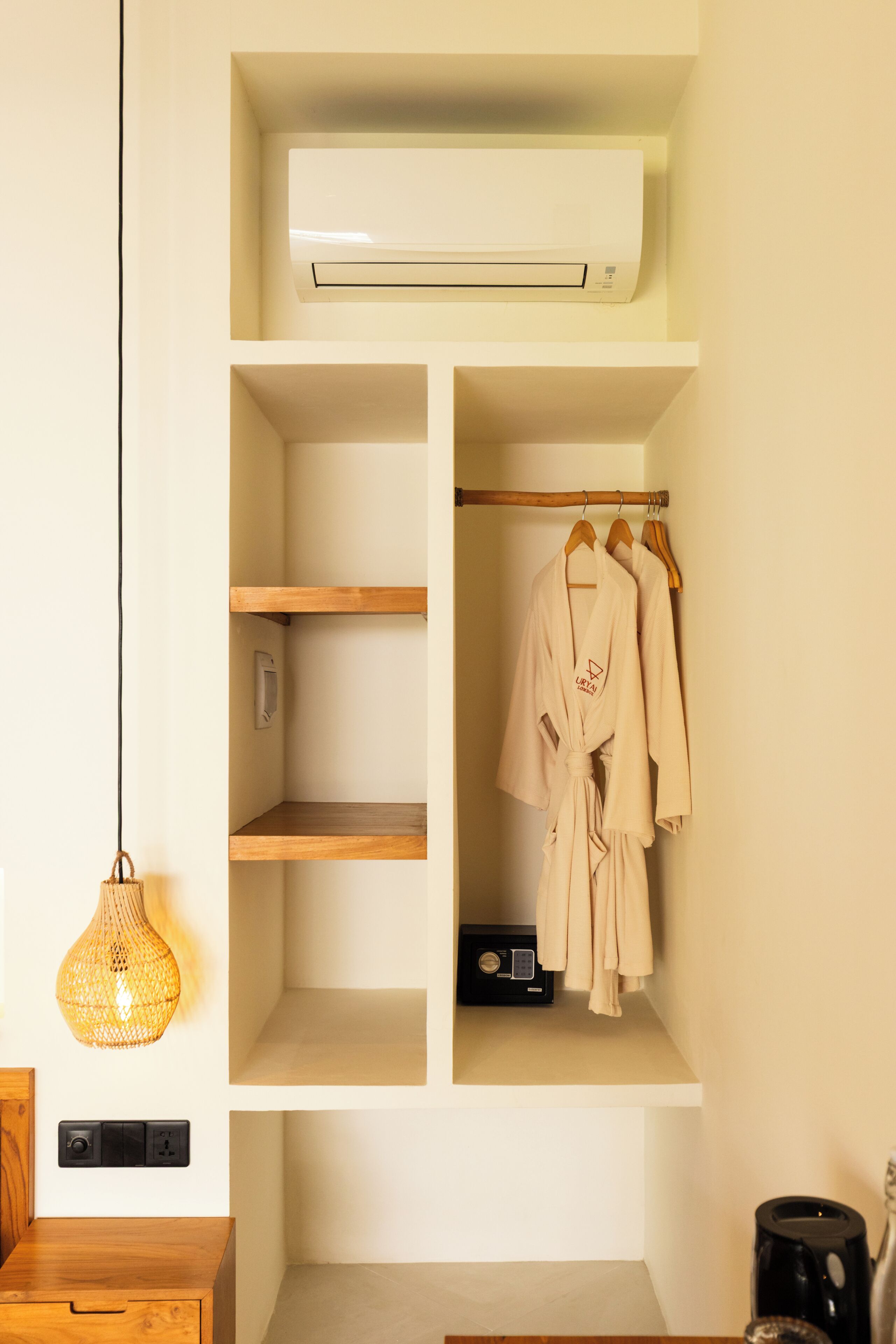 Habitación con aire acondicionado integrado, estanterías de madera, lámpara colgante y perchero con batas.