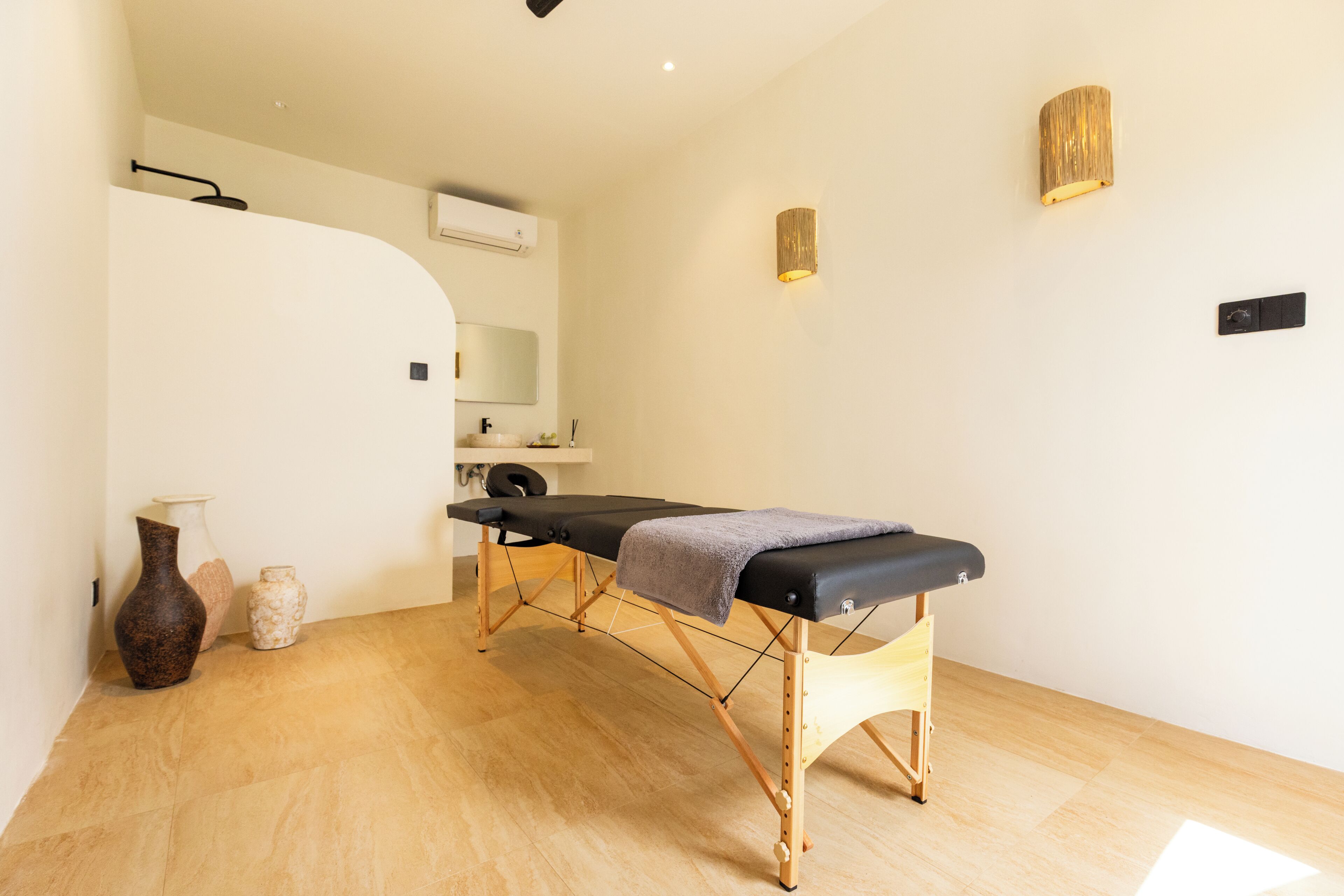 Une salle de soins dotée d’un plancher en bois, d’une table d’examen noire, d’un miroir et d’un luminaire fixé au mur.