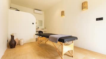 Une salle de soins dotée d’un plancher en bois, d’une table d’examen noire, d’un miroir et d’un luminaire fixé au mur.
