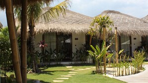 A resort with thatched-roof structures, a paved walkway, and tropical plants. - Uryah Hotel Lombok (Selong Belanak)