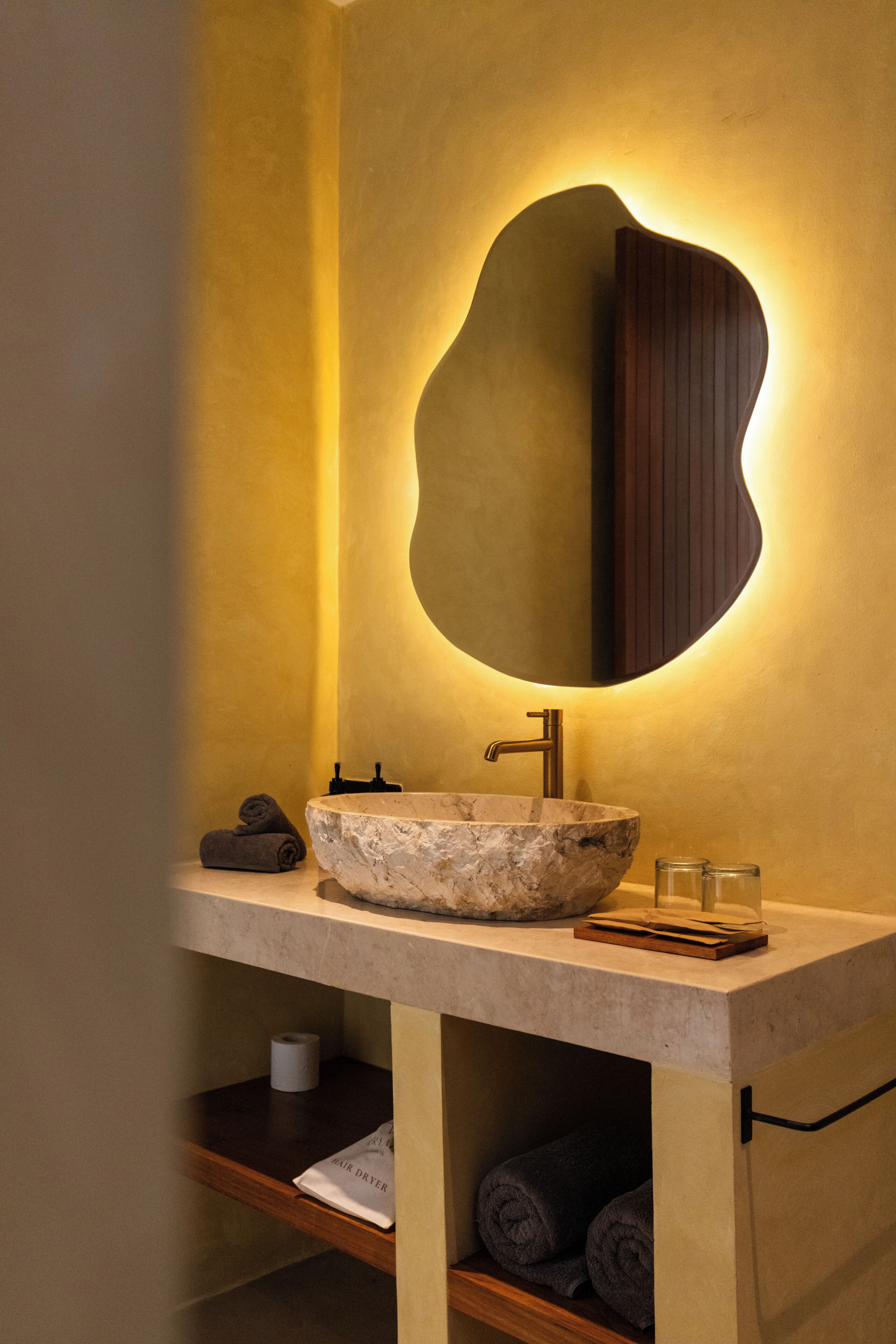 A bathroom with a large, round, marble sink, a modern mirror, and a towel rack.
