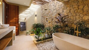 A modern bathroom with a freestanding bathtub, a wooden vanity, and a stone wall. - Uryah Hotel Lombok (Selong Belanak)
