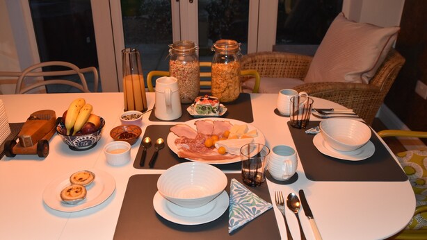 Een eettafel gedekt met verschillende gerechten, bestek en een rotan stoel op de achtergrond.