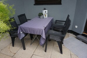 Un patio al aire libre con una mesa cubierta por un mantel morado, rodeado de sillas negras.