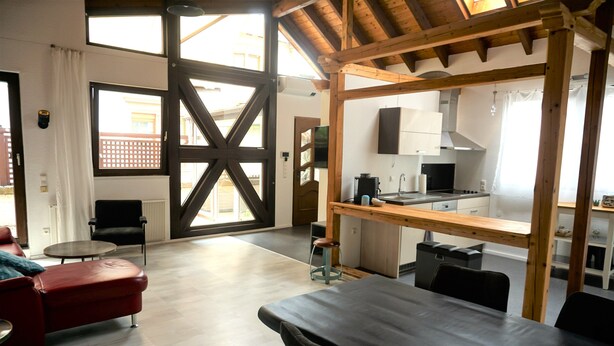 A spacious living area with a large window, a red sofa, a wooden table, and a kitchen in the background. - The very special vacation apartment (Bingen am Rhein)