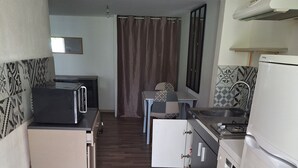 Cocina compacta con microondas, pileta y refrigerador. Se observa un pequeño comedor con una mesa y sillas al fondo.