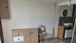 Un dormitorio con cama, un mueble de madera con cajones, una silla, un radiador y un espejo sobre un lavabo.