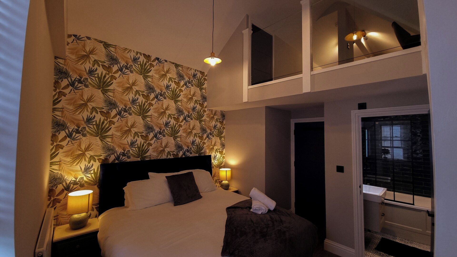 A bedroom with a bed, two bedside lamps, a nightstand, a mirror, and a window with a view.