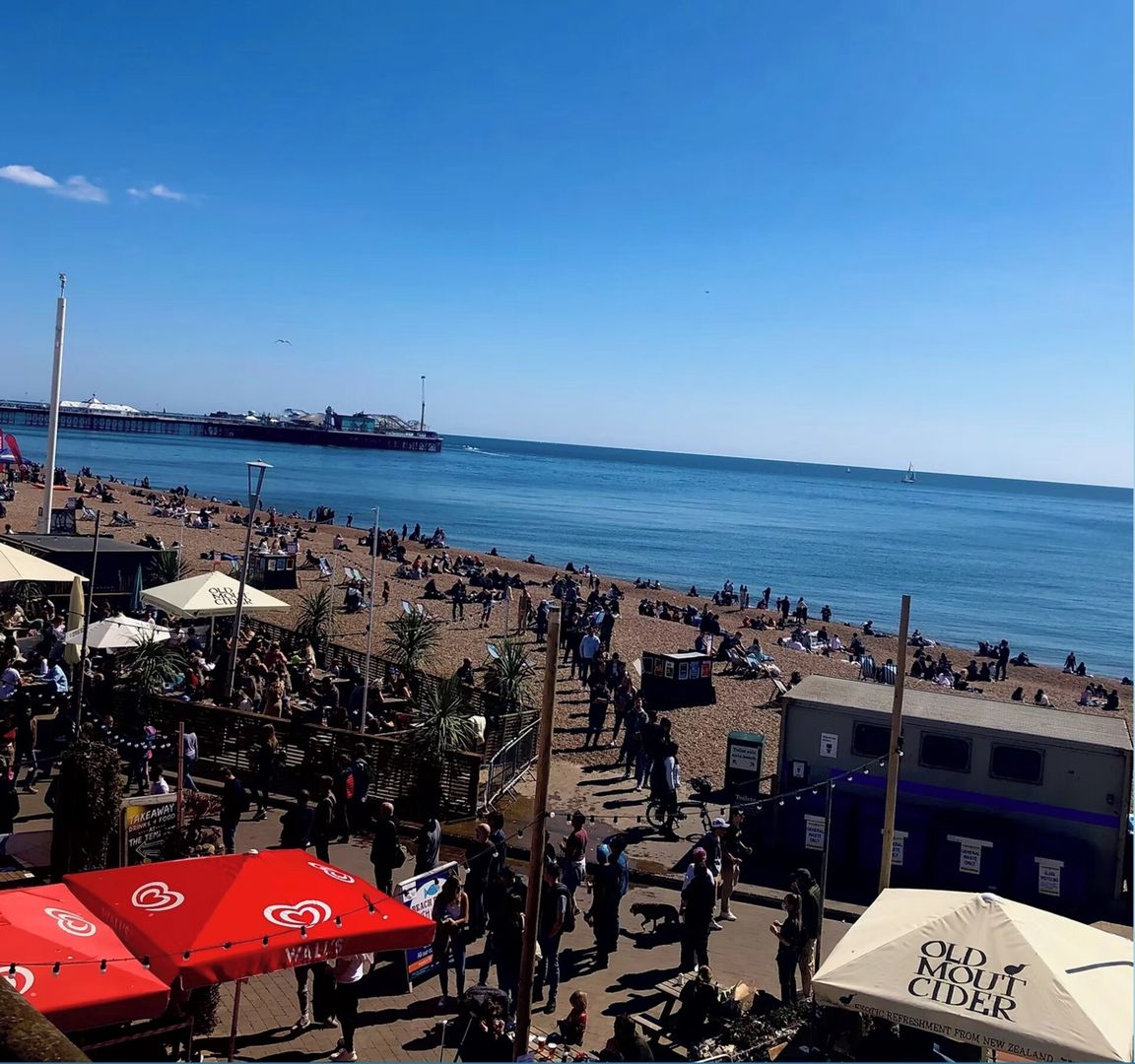 Une plage avec des gens, des parasols et une jetée en arrière-plan.