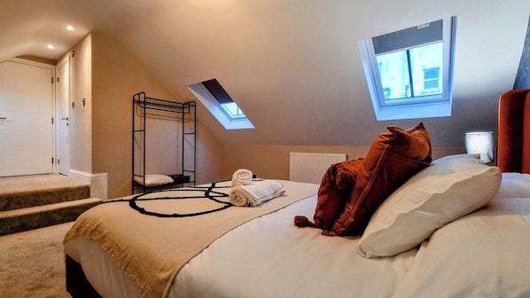 A bedroom with a bunk bed, a skylight, a bed with a blanket, and a window.