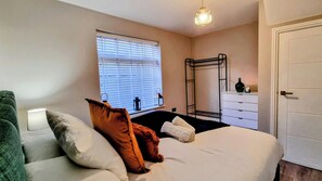 A bedroom with a bed, pillows, a window with blinds, a bedside table, a wardrobe, and a hanging light fixture. - Heart of Brighton: 4 Bed, 4 Bath + Parking (Brighton and Hove)