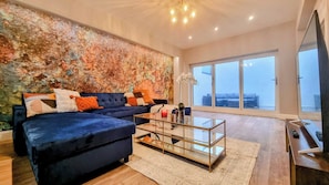 A modern living room with a sectional sofa, a glass coffee table, and a large window offering a city view.