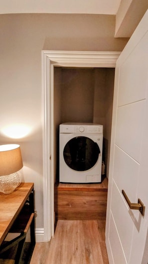 A laundry room with a washing machine, a wooden floor, and a door with a brass handle.