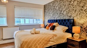 Un dormitorio con una cama grande, un papel tapiz decorativo y una ventana con persianas.