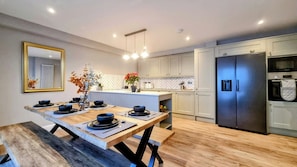 A modern kitchen with a wooden dining table, white cabinets, and a stainless steel refrigerator. - Heart of Brighton: 4 Bed, 4 Bath + Parking (Brighton and Hove)