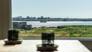Vista desde una ventana sobre un cuerpo de agua con un barco, edificios y vegetación.