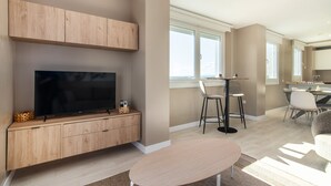 Una sala de estar moderna con televisor de pantalla plana, muebles de madera, un área de comedor con mesa y sillas, y un ventanal con vistas.