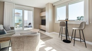 Una sala moderna con sofá, comedor con dos sillas, televisor y zona de cocina.