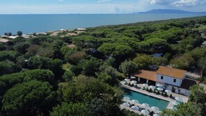 Vue aérienne d’un complexe hôtelier avec une piscine, des chaises longues et une vue sur la mer.