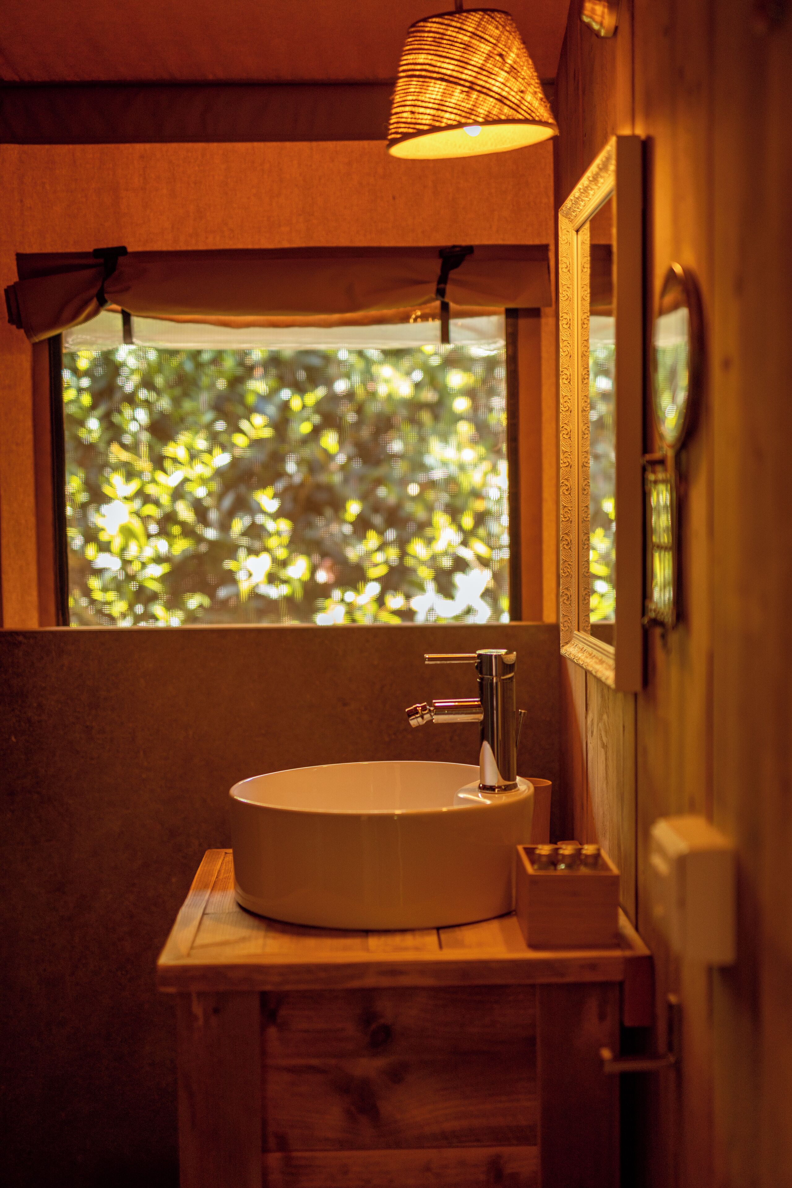 Une salle de bain avec un meuble-lavabo en bois, un lavabo rond, un miroir et une fenêtre donnant sur un paysage verdoyant.