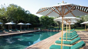 A swimming pool with lounge chairs and striped umbrellas. - Resort & Glamping Terre di Sacra (Capalbio)