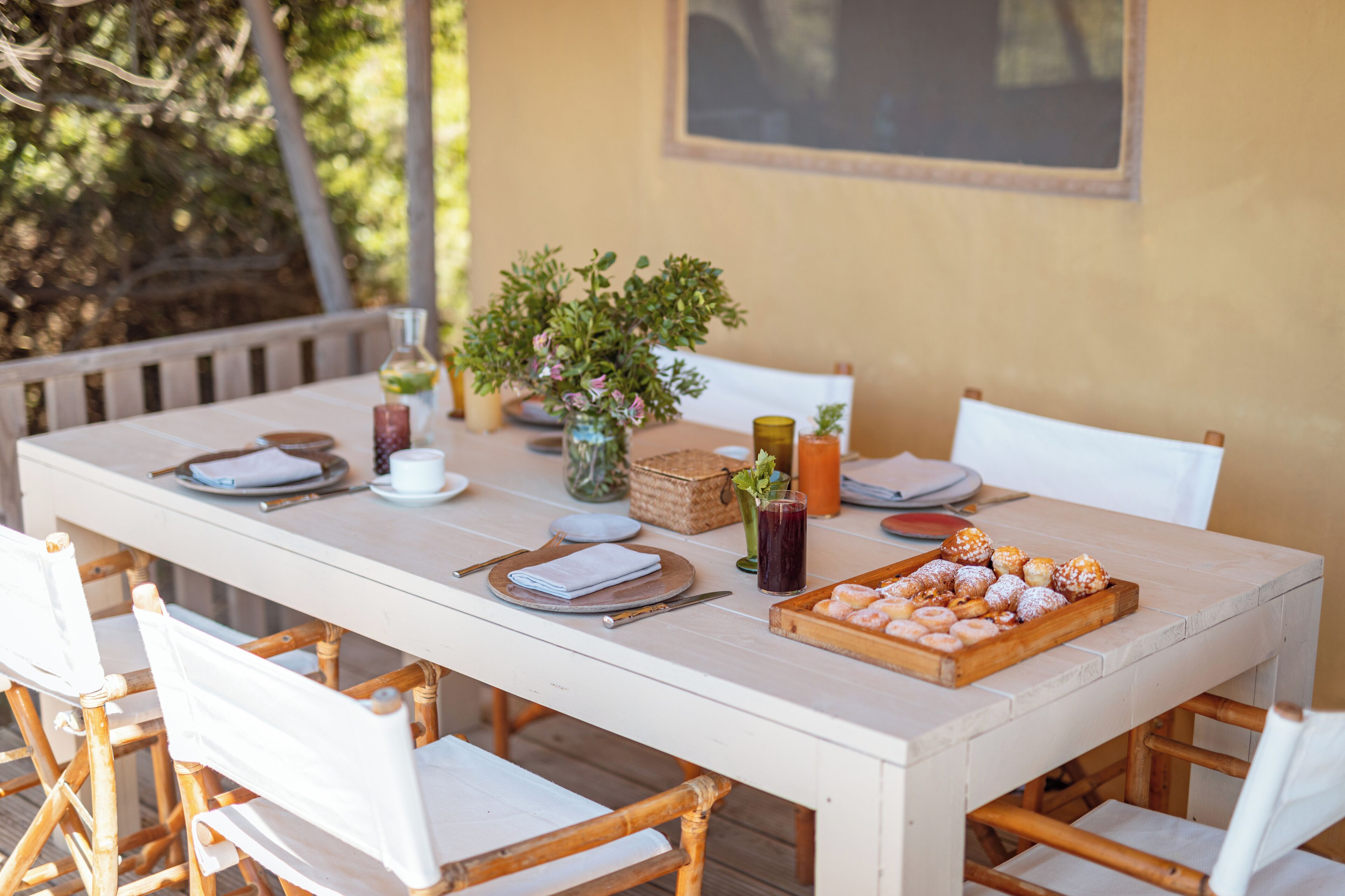 A dining table set with plates, cutlery, a vase with flowers, a drink, and a tray of pastries.