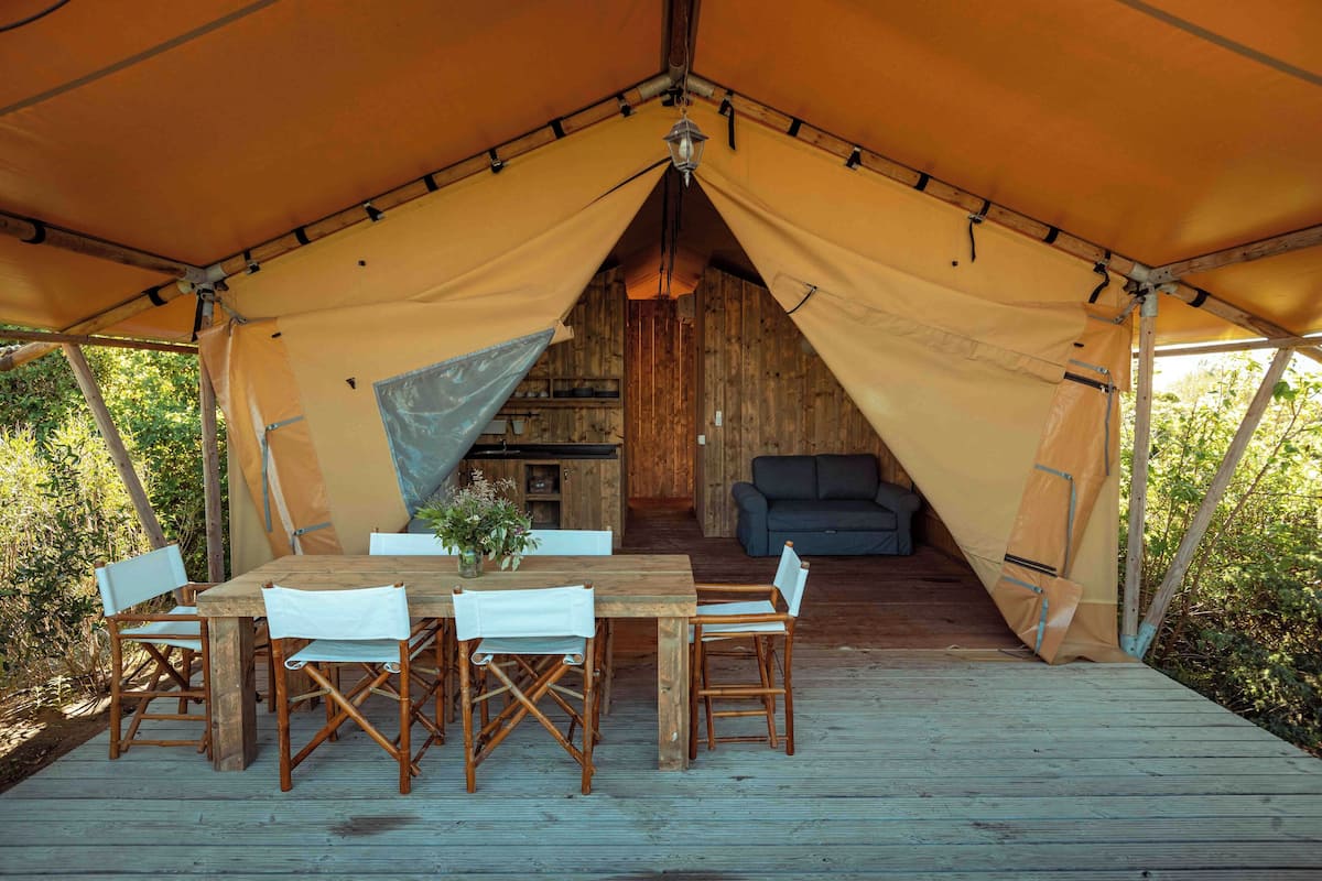 Una tienda de campaña con una terraza de madera, una mesa de comedor con sillas y un sofá en el interior.