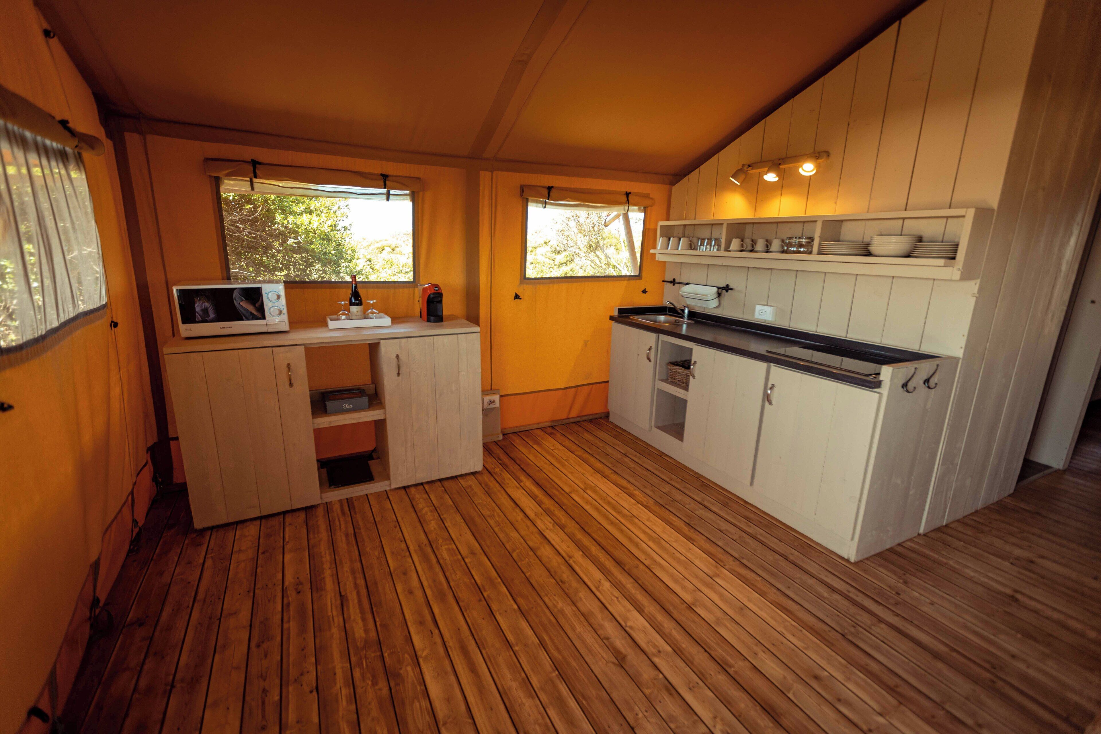 A compact kitchen with wooden flooring, built-in cabinets, and a microwave.
