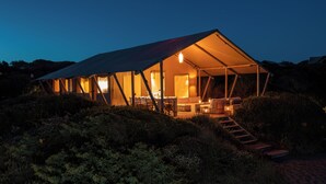 A tented accommodation with a dining area, a staircase, and a view of the surrounding landscape. - Resort & Glamping Terre di Sacra (Capalbio)