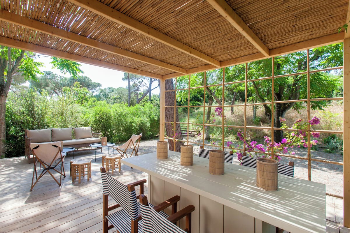 Un espacio de estar al aire libre cubierto con terraza de madera, un sofá, sillas y una mesa con macetas.