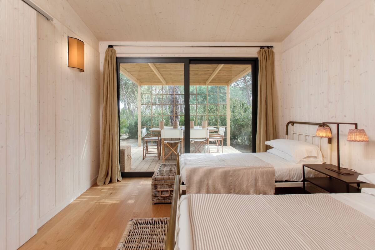 Un dormitorio con dos camas, una mesa y sillas, y vistas al exterior.