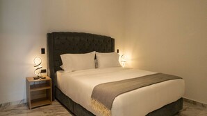 A neatly made bed with a dark headboard, two bedside tables with wall-mounted lamps, and a marble floor.