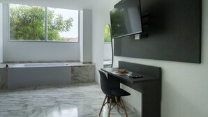 A modern bathroom with a marble floor, a bathtub, and a large window with a view of trees.
