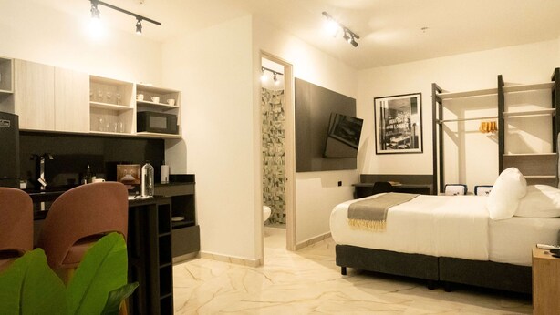 A modern hotel room with a bed, a desk, and a TV. There is a bathroom visible through a door. - w *|Cozy 1BR w/ AC near Ciudad Amurallada (Cartagena de Indias)