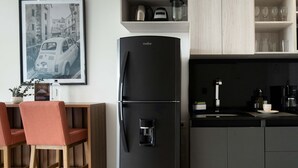 A modern kitchen with a black refrigerator, wooden chairs, and a coffee machine.