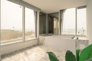 Ein modernes Badezimmer mit einer großen Badewanne, Marmorböden und großen Fenstern mit Meerblick.