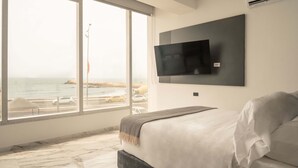 Quarto moderno com uma janela grande, televisão de tela plana fixada na parede e cama com manta cinza.