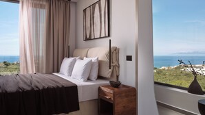 A bedroom with a bed, a nightstand, a vase, and a view of the sea.