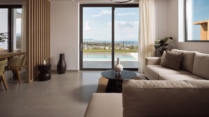 A modern living room with a large window, a sofa, a dining table, and a view of a pool and landscape.