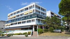 Un edificio de varios pisos con balcones, un acceso cubierto y un automóvil cerca.
