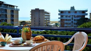 Un balcón con una mesa lista para el desayuno, con vistas a la playa y edificios.