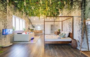 Una habitación con cama, televisor, escritorio y una pared decorada con plantas colgantes.